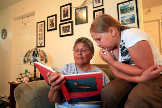 Cancer patient Emma Michael shows her granddaughter Donya Wandering Spirit a family photo album at her home in Fort Chipewyan, northern Alberta, 2009. Mrs Michael survived an aggressive breast cancer tumor and believes that her cancer was caused by increased levels of pollution to the air and water downstream from the tar sands sites. Five of her relatives, displayed on the wall behind her, have died of various forms of cancer in recent years.