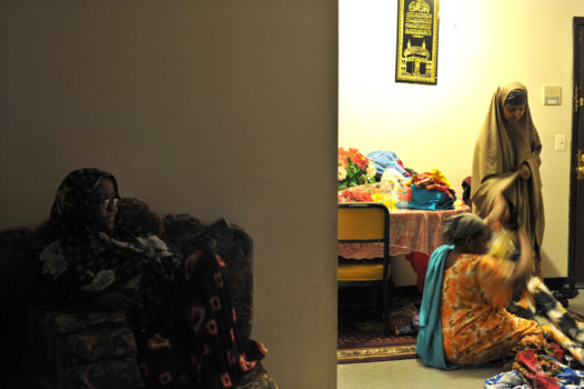 Hamdi watches TV in her home while her mother sells traditional clothes to a neighbor. Hamdi came to the USA when she was just ten years old, so she has grown up balancing between keeping traditions of her parents and forging her own identity.