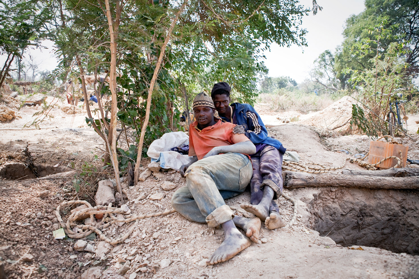 A two man team of migrant miners from Guinea relax next to their mine shaft in Senegal. Each takes it in turns to go down the 10 meter shaft for up to one hour at a time to extract gold-bearing rocks.