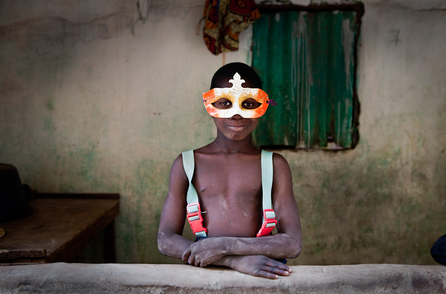 A young boy plays 'dress-up' with a Mardi Gras-style masque in the village of Mandinari, a populous settlement on a 'bolon' (tributary) off the River Gambia.