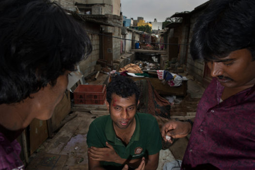 Maya stands with friends outside his home over open sewage. Men from struggling rural communities pour into Indian cities alone looking for wages with which to support their families back home. The rapists from the infamous deadly bus gang rape in Delhi of December 2012 were among this migrant population forced to inhabit slums where brutalizing conditions are the norm.