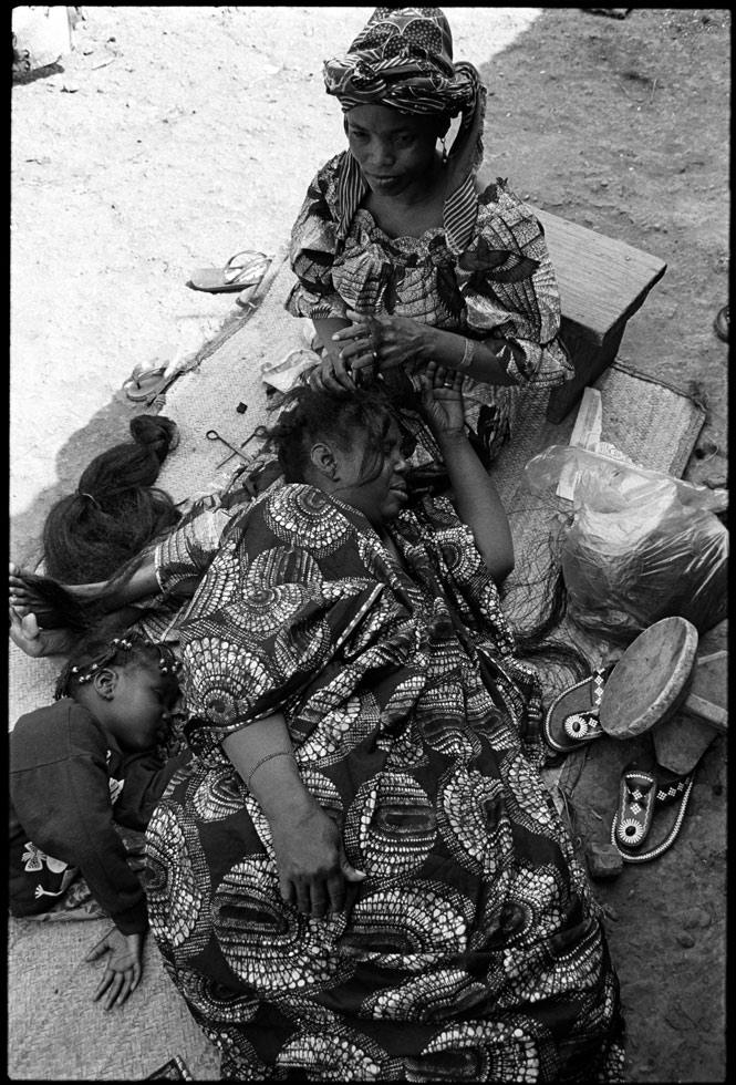 "The wise do not comb themselves; if they do, they get hurt." Ugandan proverb

A woman is having her hair styled. As it will take several hours, she makes herself comfortable, along with her daughter. Women in Mali have a sophisticated sense of fashion, particularly in terms of their clothes and hairstyles. The cheapest place to have their hair done is in the open-air market, where a large, covered shed is devoted to this trade.

Bamako, Mali, 1992