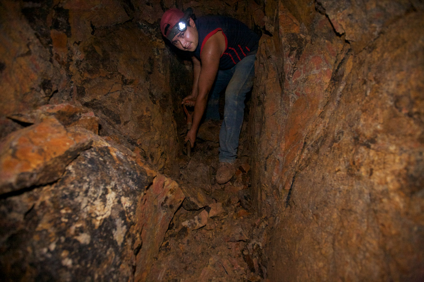 A young gold miner underground shovels gold ore in a tunnel. The small-scale miners have no equipment, it is forbidden by the terms of the concession to Canadian mining corporation 'B2 Gold' which allows only 1% of the mining to be done by small-scale miners.