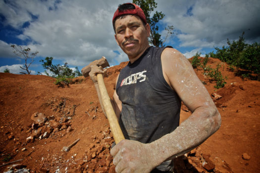A miner breaking gold ore rocks with a sledgehammer.