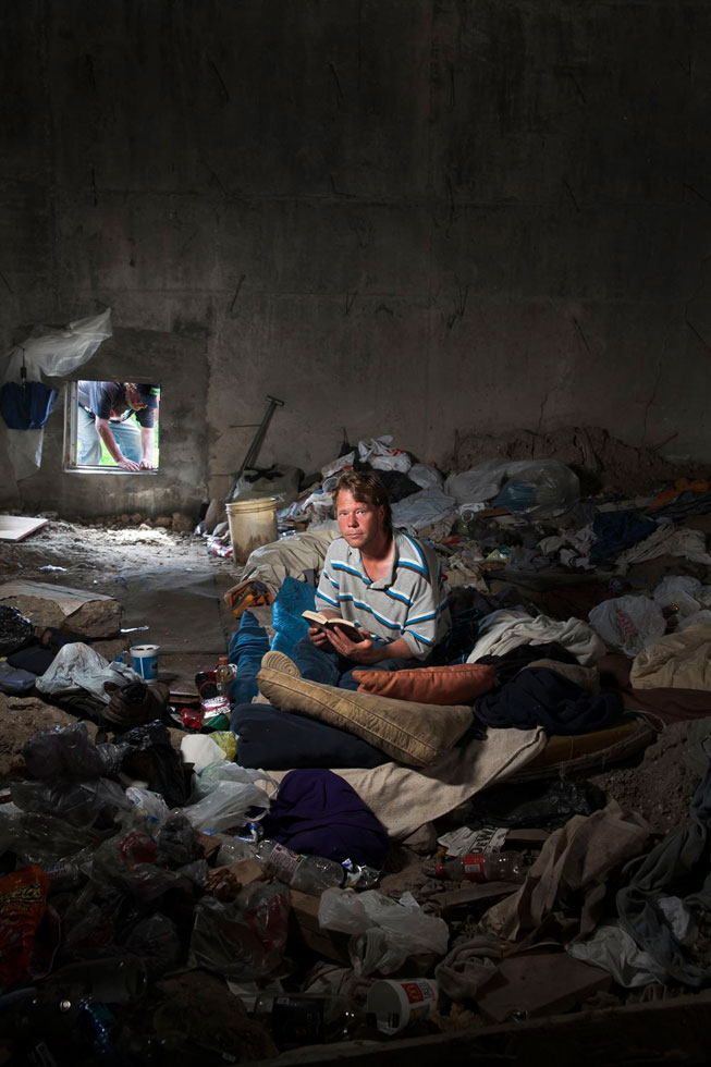 This room inside a highway exit ramp has a constant temperature of around 60 degrees, which makes it comfortable year-round. The man who lives inside this bridge did not want to be photographed for fear that he could lose his job as a crane operator. One of his friends at the camp is photographed sitting on his bed as another buddy tries to fit through the small entrance.