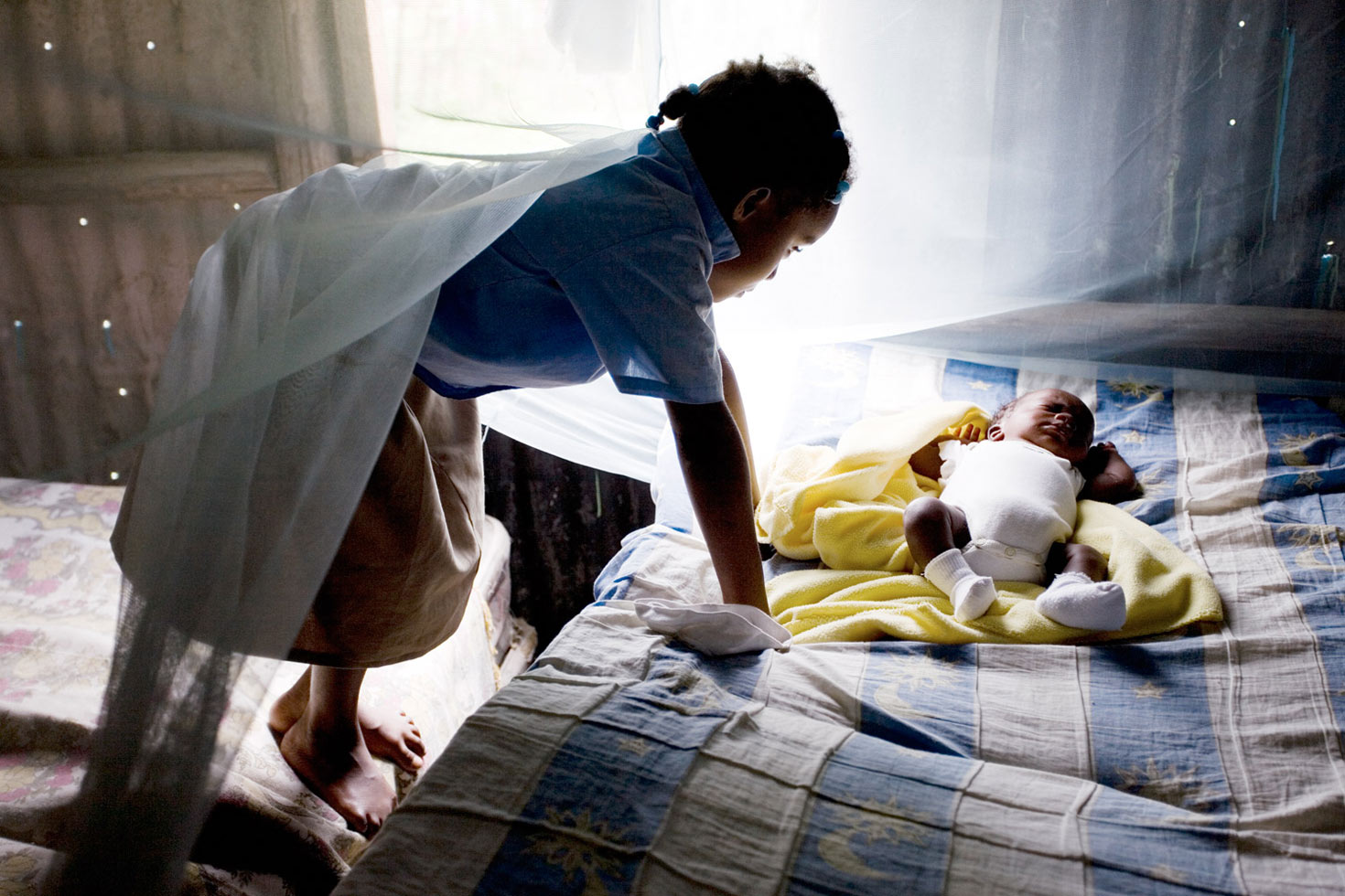Aida Valdez, 6, looks at her two-month-old cousin, Samuel, who was born three months prematurely but is now a healthy, growing "hombrecito" (little man). In Las Pajas, mosquito nets are considered a luxury that few can afford, but the nets are vital in controlling outbreaks of malaria and the infamous dengue fever.