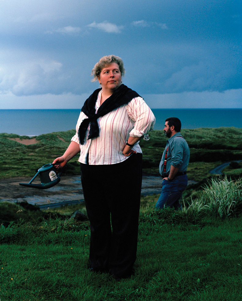 Moira Milne, Hermit Point. 

“The actual destruction of this area was brought home to me one day when bulldozers arrived and ripped out the young wood directly in front of my home, that’s the patch of earth behind me in the picture. The waste of it all was that they were taken away on trucks to further south on the estate and just buried in a hole that they had dug the previous day.

They now have problems with water lying there and they wonder why; trees drink lots of water.

This is just one example of the destruction, they also wish to destroy my home, which my husband and myself have spent years extending through our married life and has become part of us, it’s like our baby.  We have built it with our own hands, it has our blood sweat and tears in the walls. It’s part of us and cannot be replaced as it is a one off, like each and every person is.”